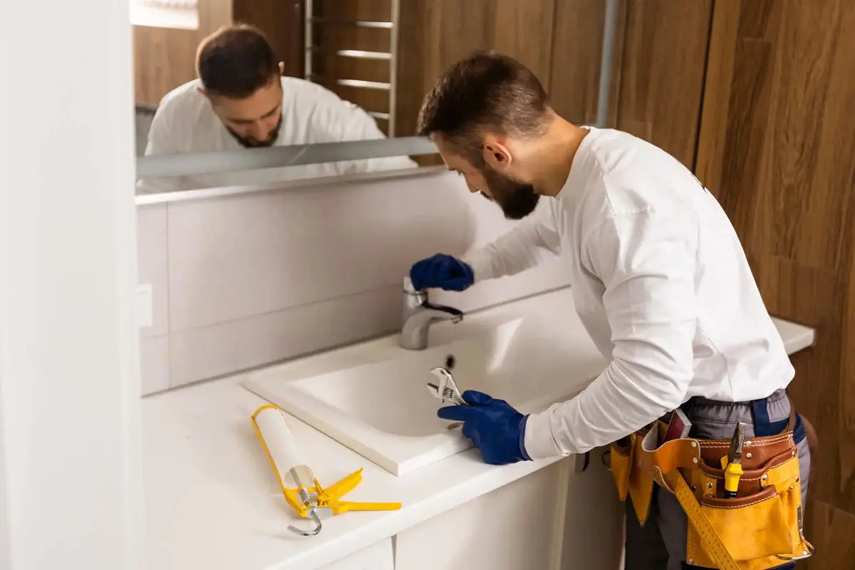 A handyman installs a bathroom sink with tools nearby.