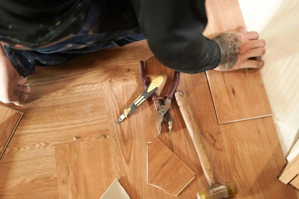 Person repairing wooden floor with hammer and nails.