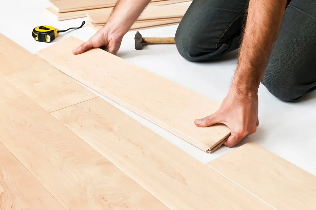 Person installing wooden flooring with hands placing a plank.