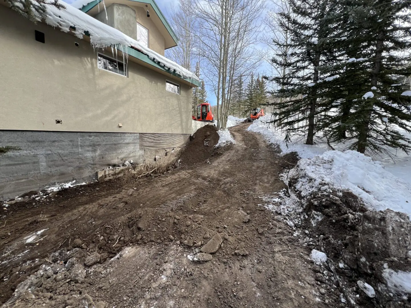 Snowy backyard with muddy pathway and construction work near house.